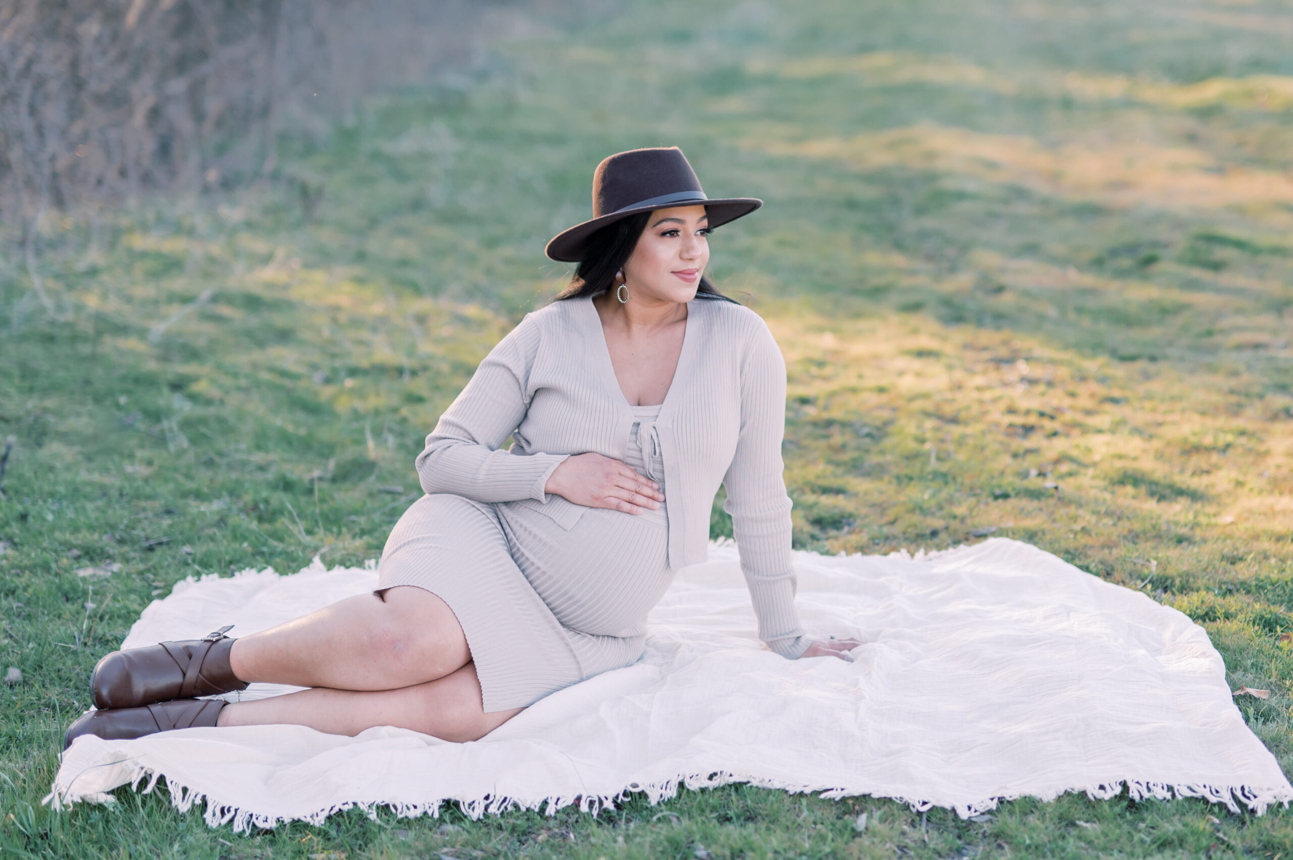 mom rests hand on pregnant belly while sitting on a blanket at a park in Fort Worth