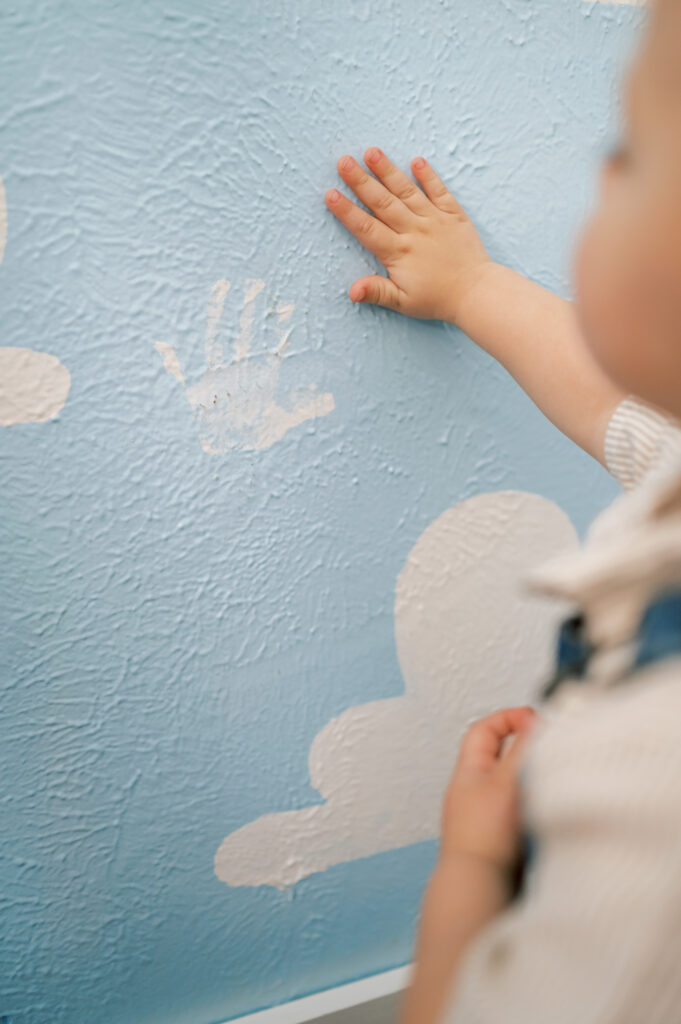 boy puts hand next to hand painted wall in bedroom