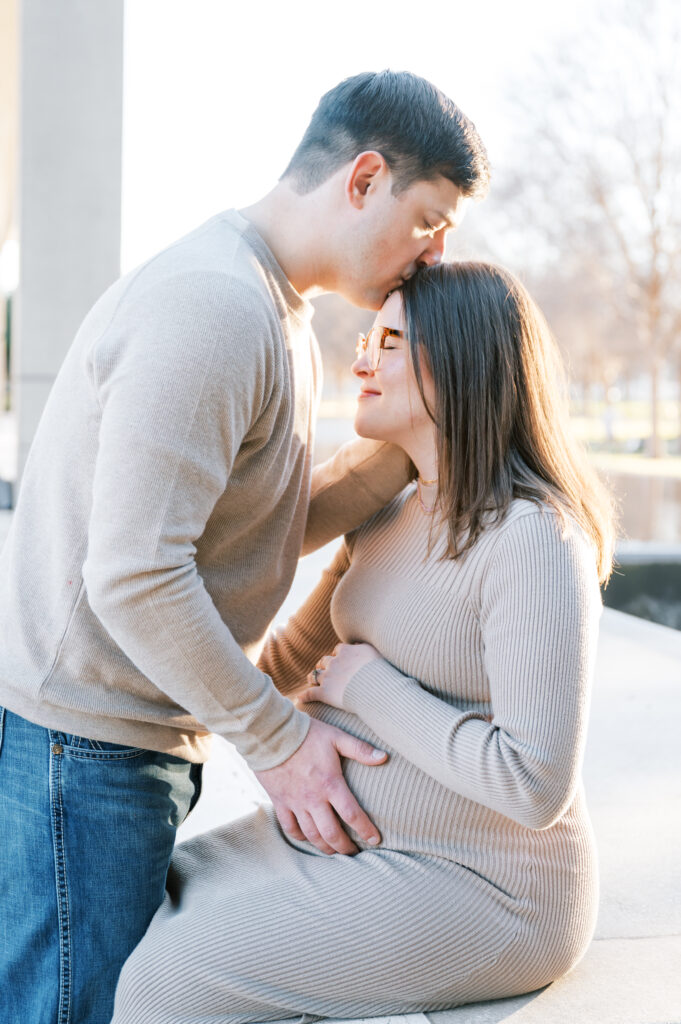 husband kisses expecting mom while touching baby bump