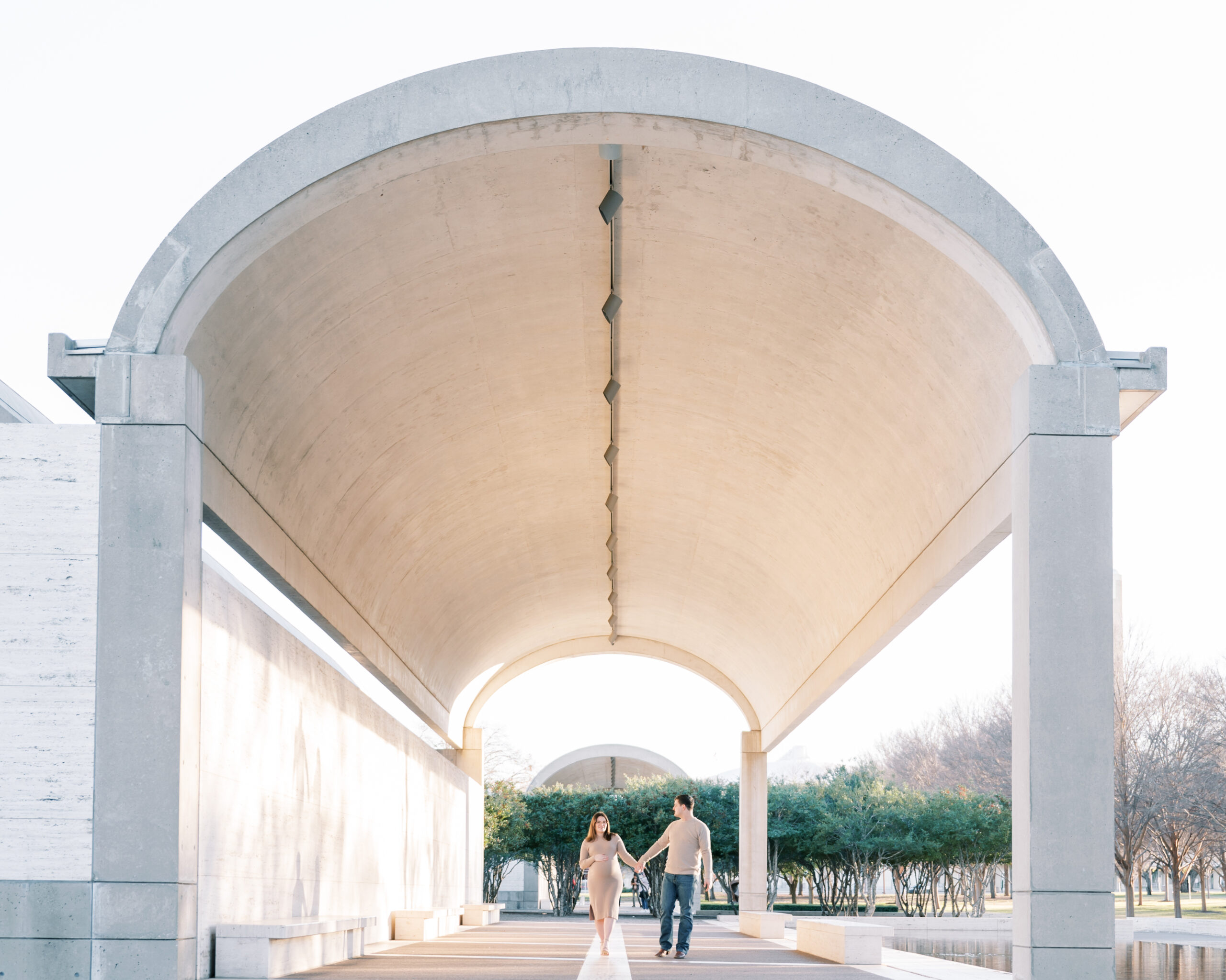 expecting mom and dad walk through the archway at the kimbell art museum