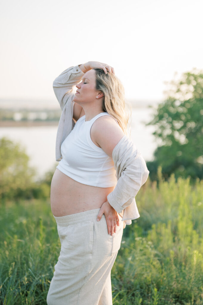 expecting mom looks up and touches hair at sunset in Fort Worth