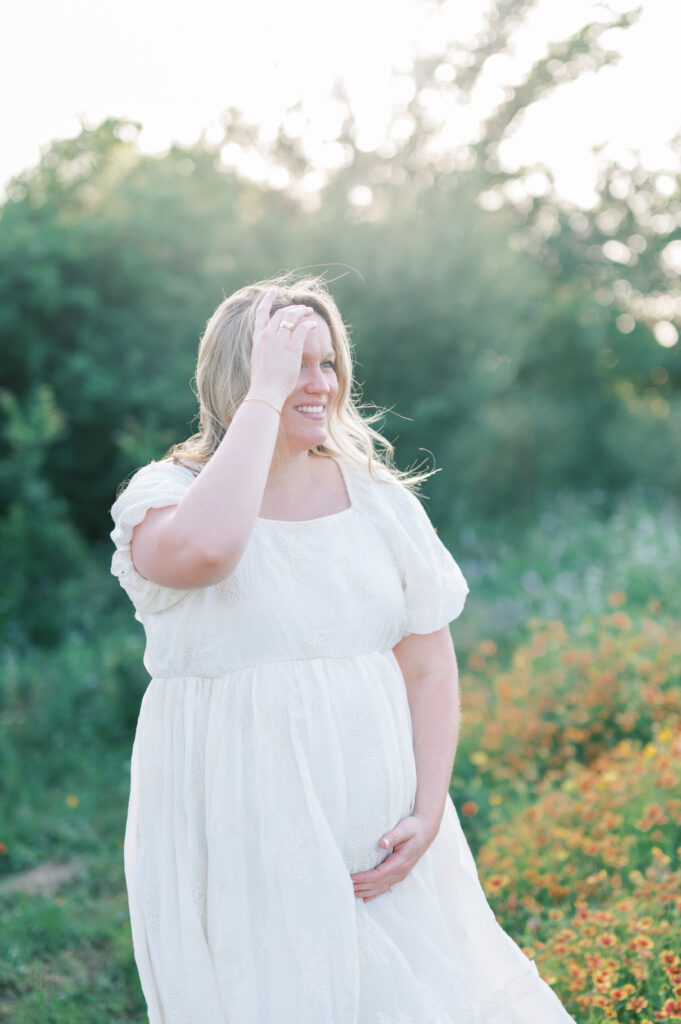 expecting mom stands in a field of flowers and sunlight