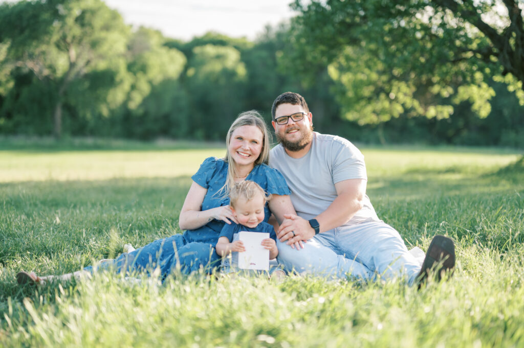 family sits in grass in a field and smiles during family photo session