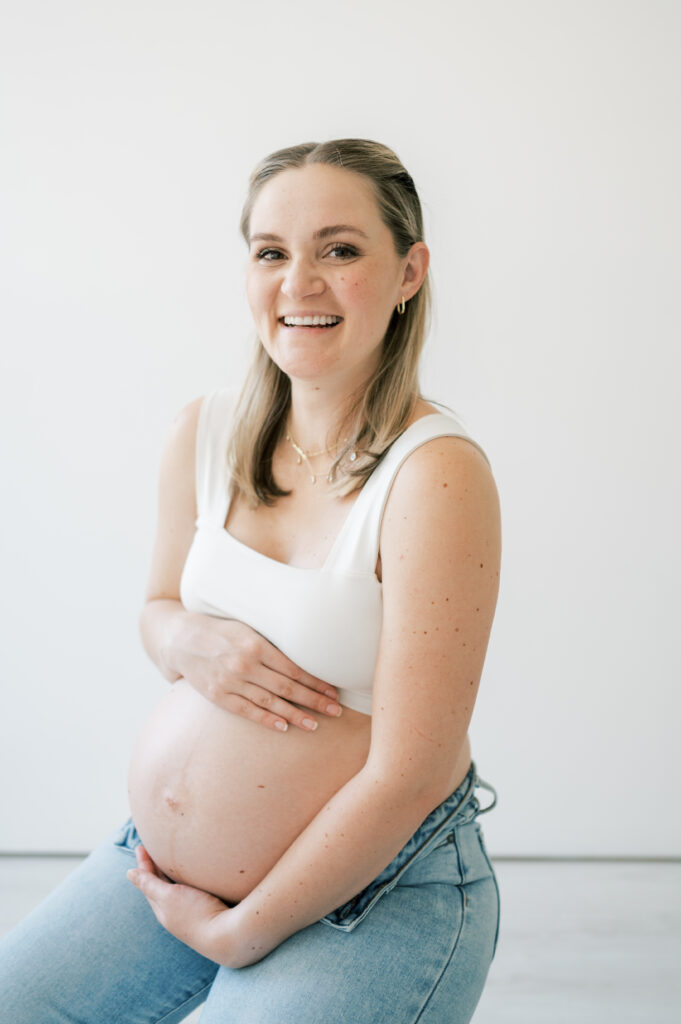 expecting mom smiles while holding baby belly bump