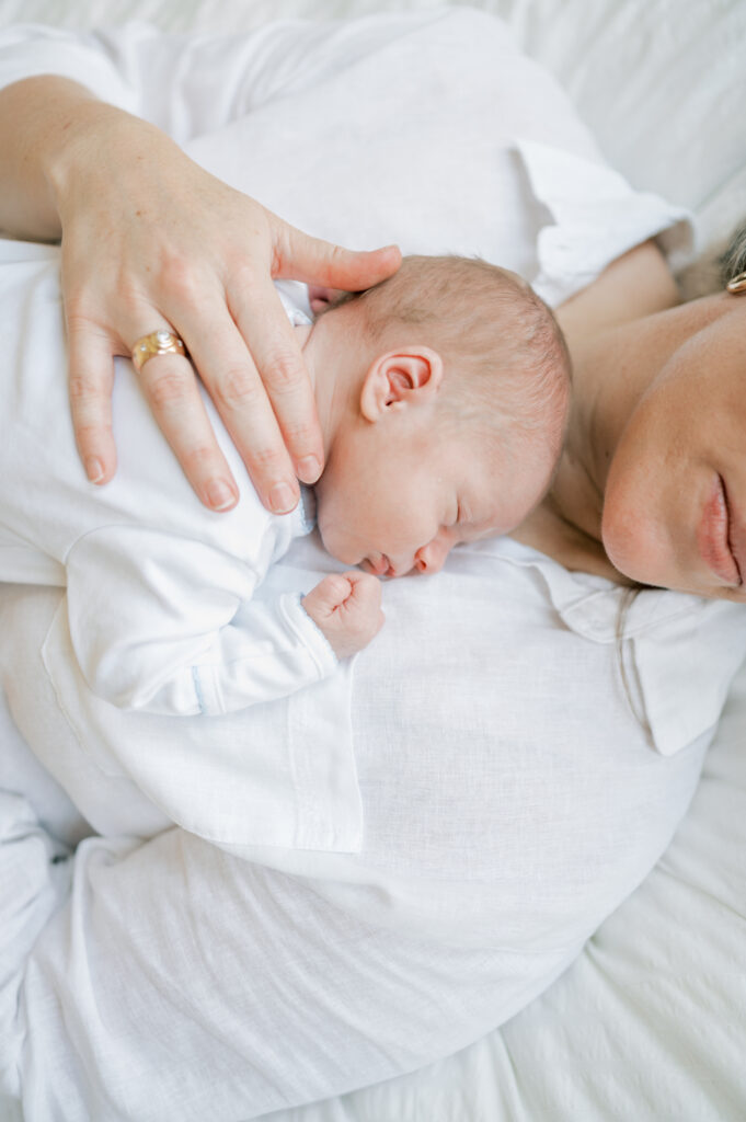 at home newborn session in fort worth - mom holds baby laying on bed