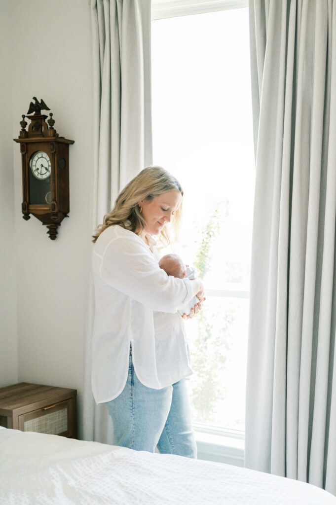 at home newborn session mom holds baby near window