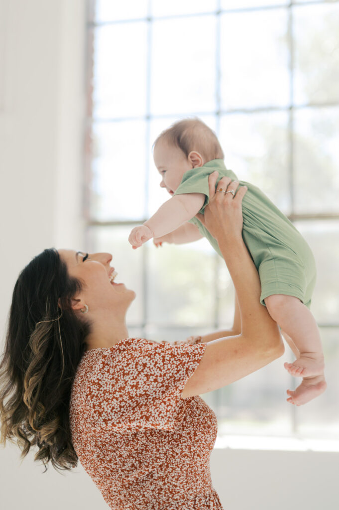 mom picks up baby boy with window in background