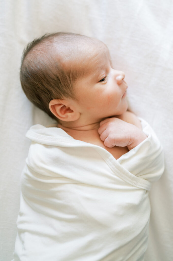 newborn baby side eyes while laying in swaddle on bed