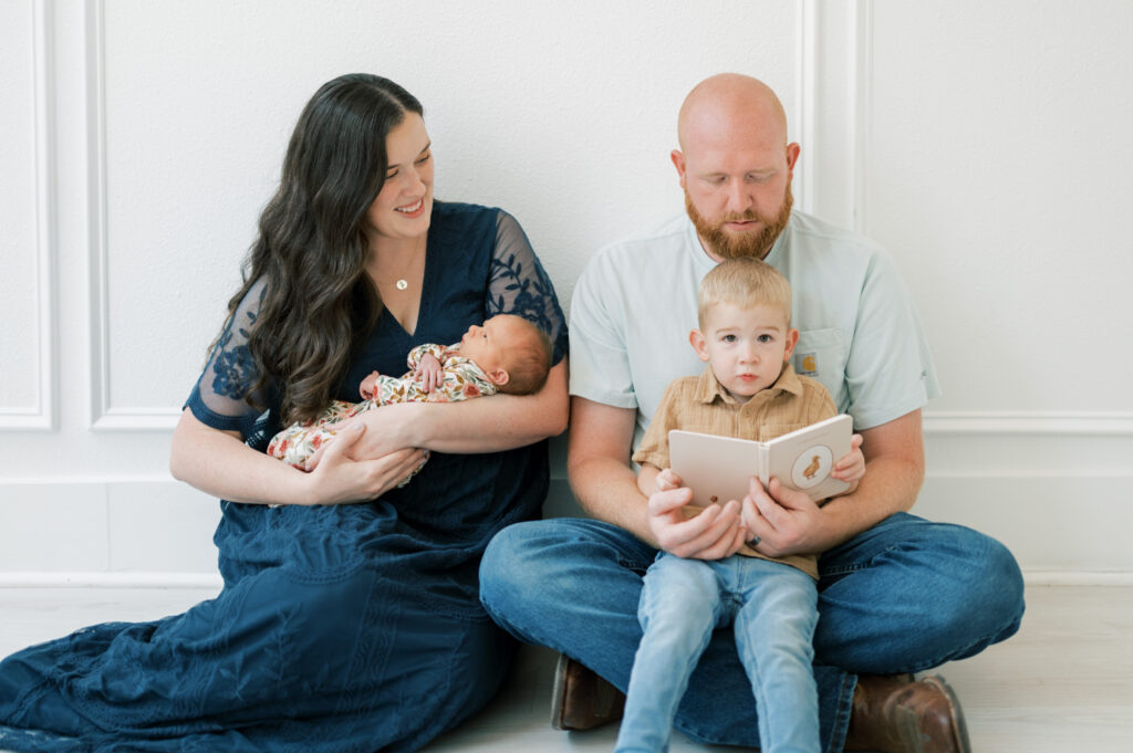family with newborn and little boy sit and read a book in a studio