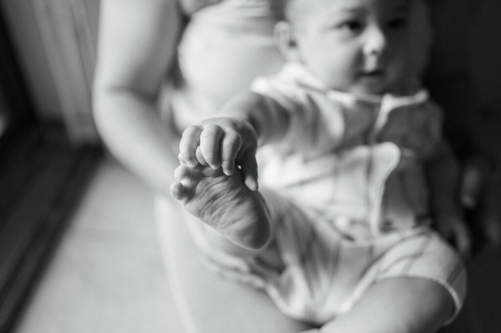 baby holding foot while sitting on mom's lap by front door