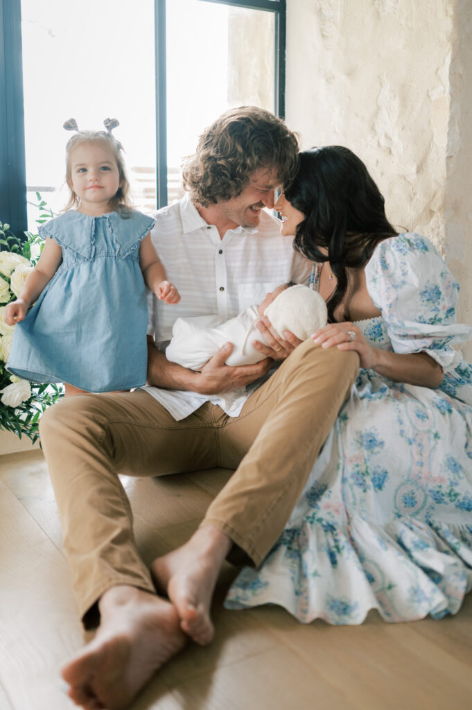 newborn photos with a family of four, mom and dad snuggles while holding newborn and older sister looks straight 