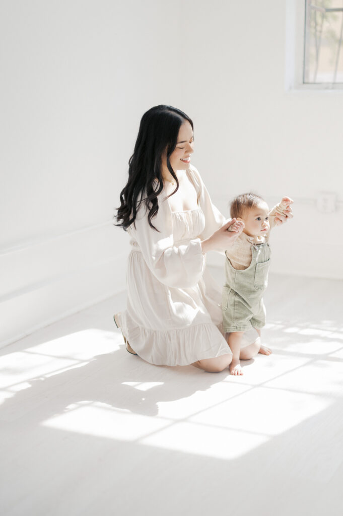 mom holds baby boy's hands while he stands 