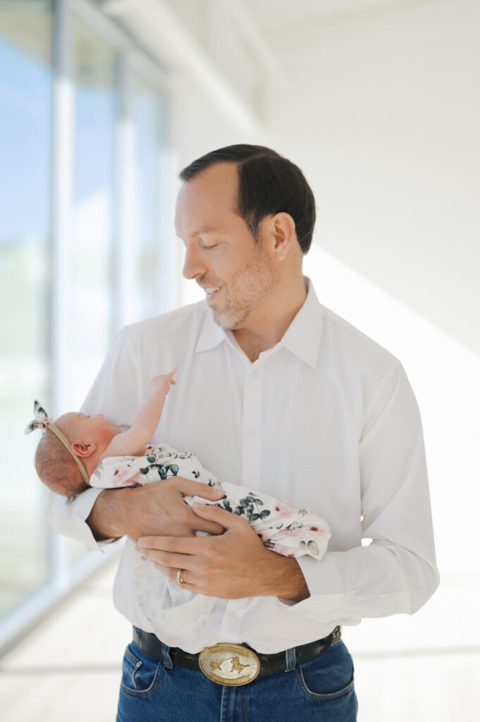 dad smiles down at newborn girl while holding her