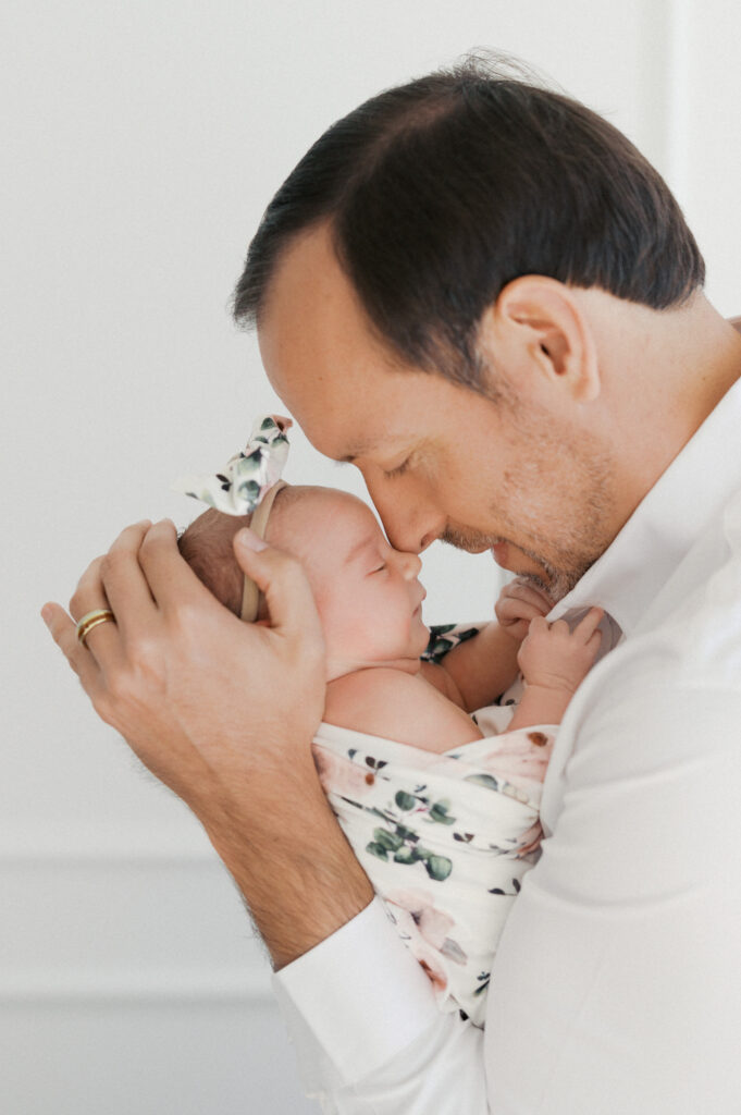 dad snuggles newborn baby girl in studio