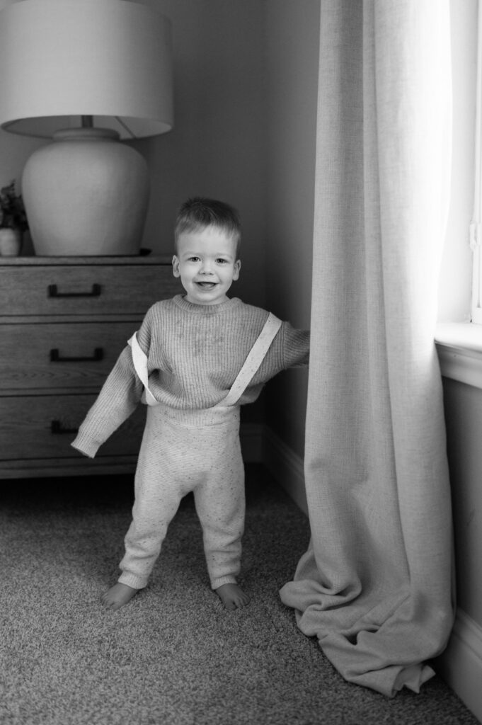 toddler smiles while hiding behind curtains