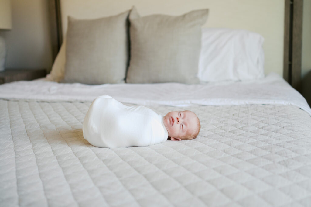 newborn lays on bed in a swaddle asleep