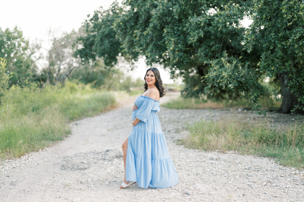 expecting mom smiles while holding baby bump during maternity photos outdoors