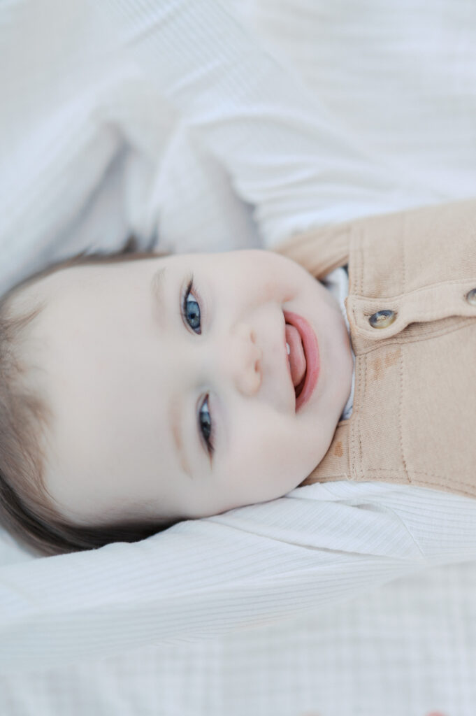 one year old boy smiles while laying on a blanket outside