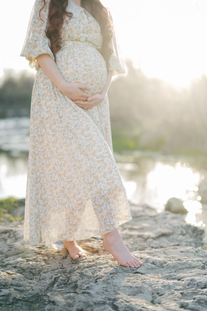 mom embraces baby bump while sun shines in background
