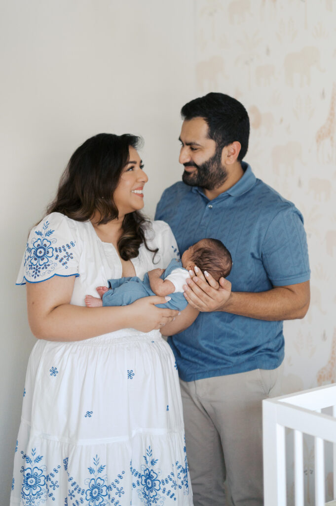 new parents smile at each other while holding newborn baby