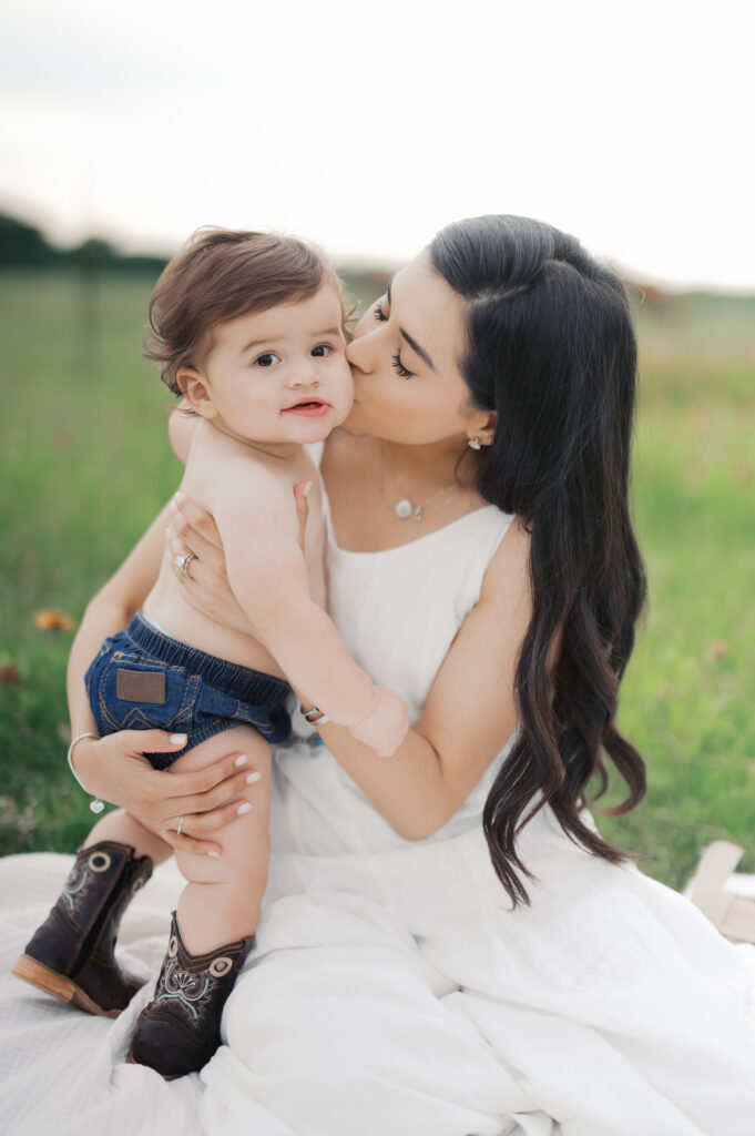 mom kisses one year old's cheeks in a field in benbrook, texas