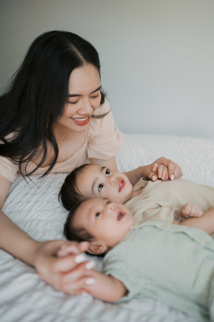 mom cuddles near kids on bed during newborn photo session