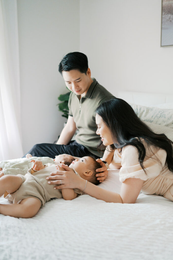 family gathers on bed during newborn photos, toddler and newborn lay on bed together