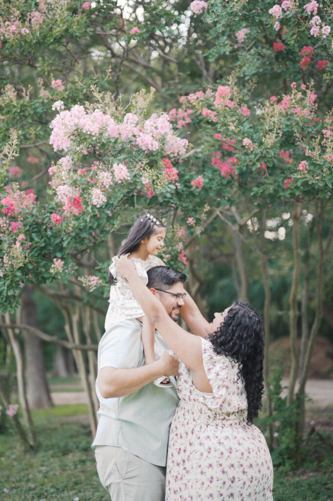 family of three stands near a blooming tree during maternity photos