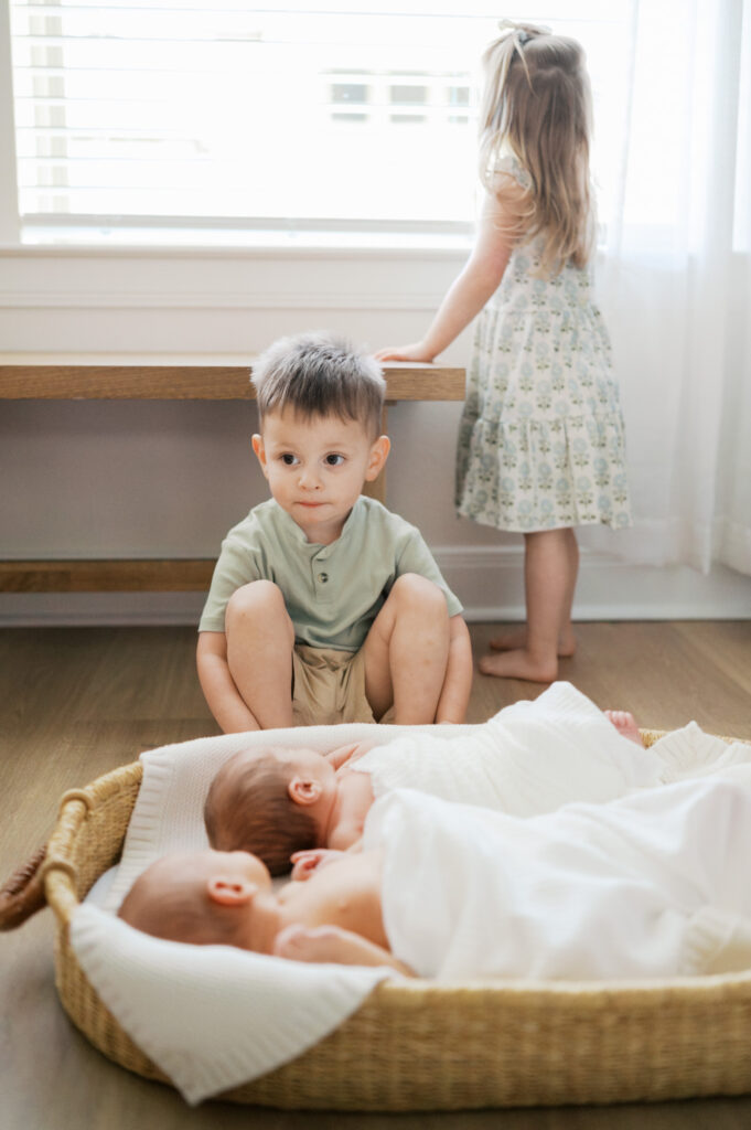 lifestyle newborn photos at home, toddlers sit and stand near new twin siblings
