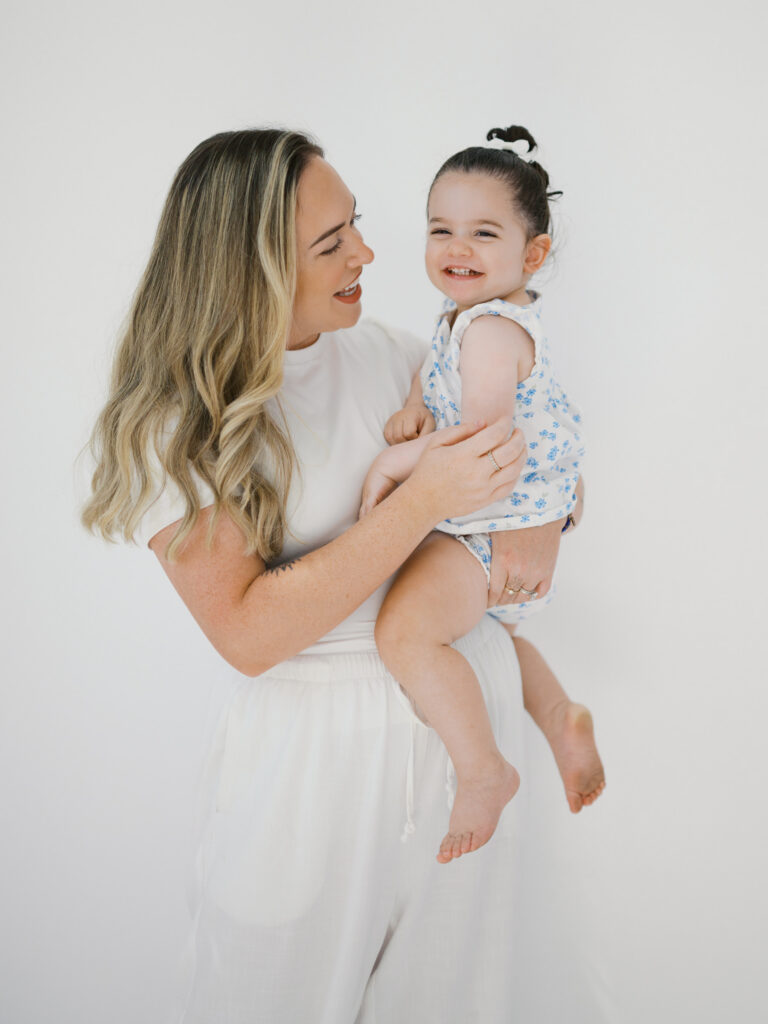 mom smiles at little girl while she giggles