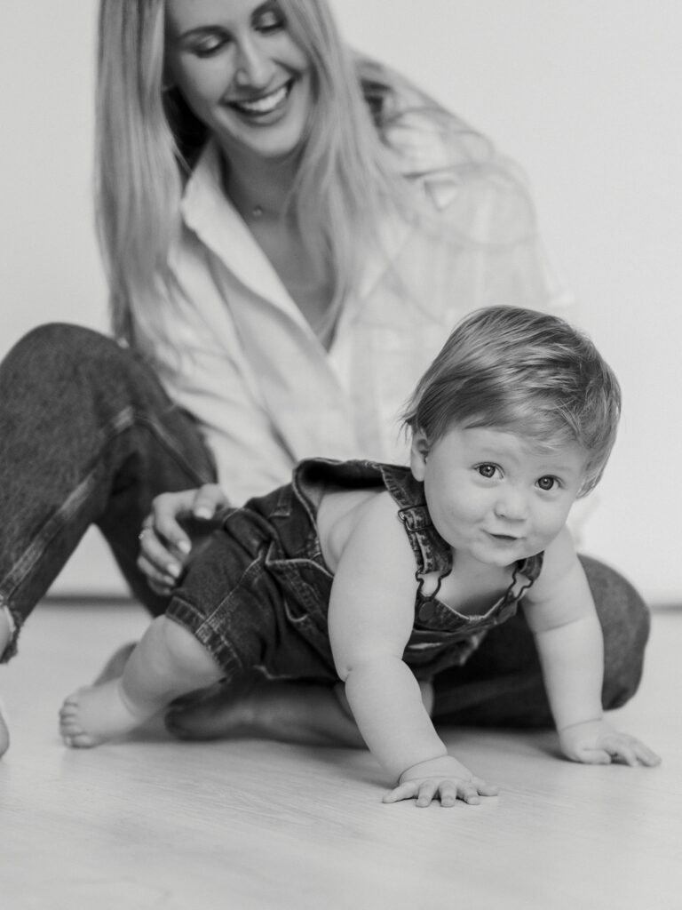 mom smiles at little boy as he crawls away during studio photos in fort worth