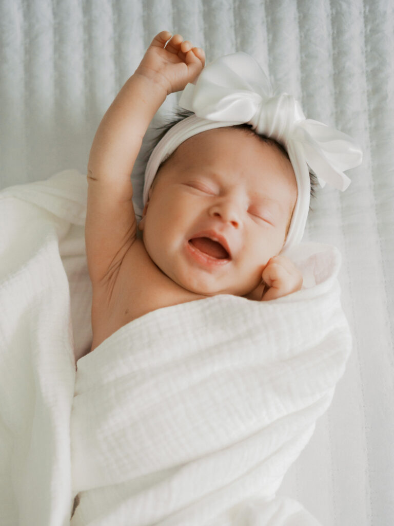 baby stretches while loosely swaddled during newborn photos
