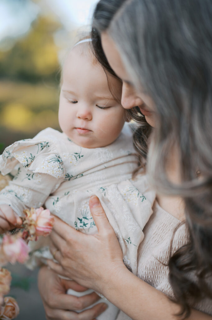 mom holds little girl while she touches a rose at the fort worth botanic garden