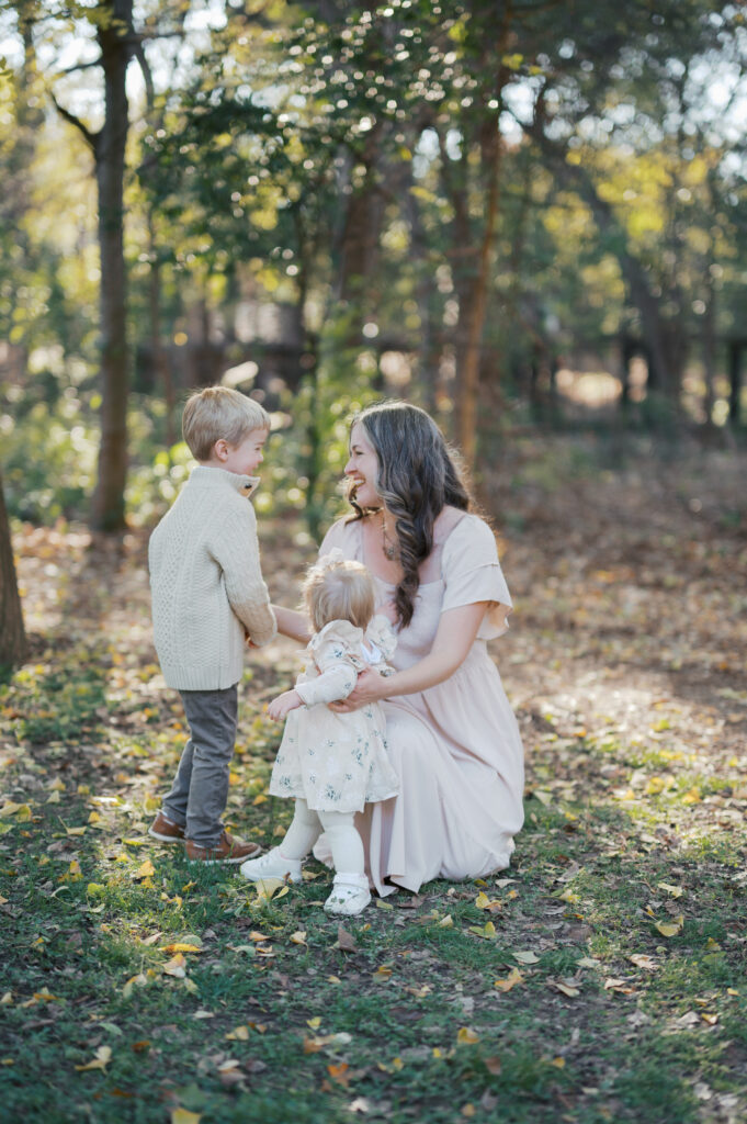 mom kneels in grass with kids outside at the fort worth botanic garden