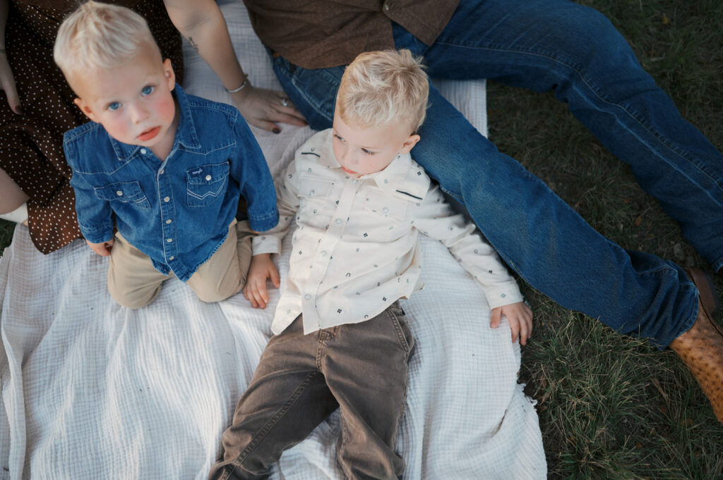 family with toddlers lays on blanket outside for family photos