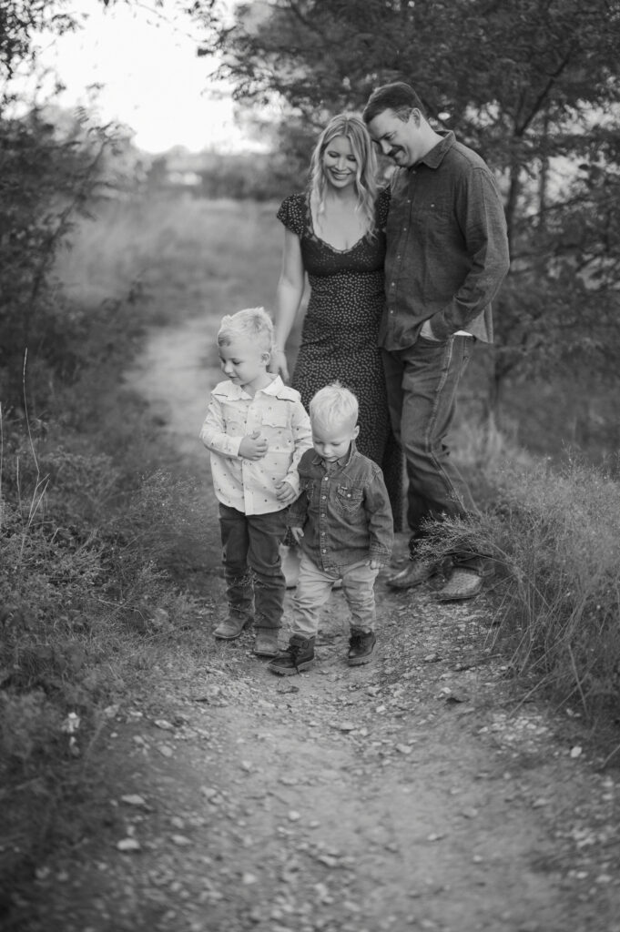 mom and dad look down happily at toddler boys outside during family photos in fort worth