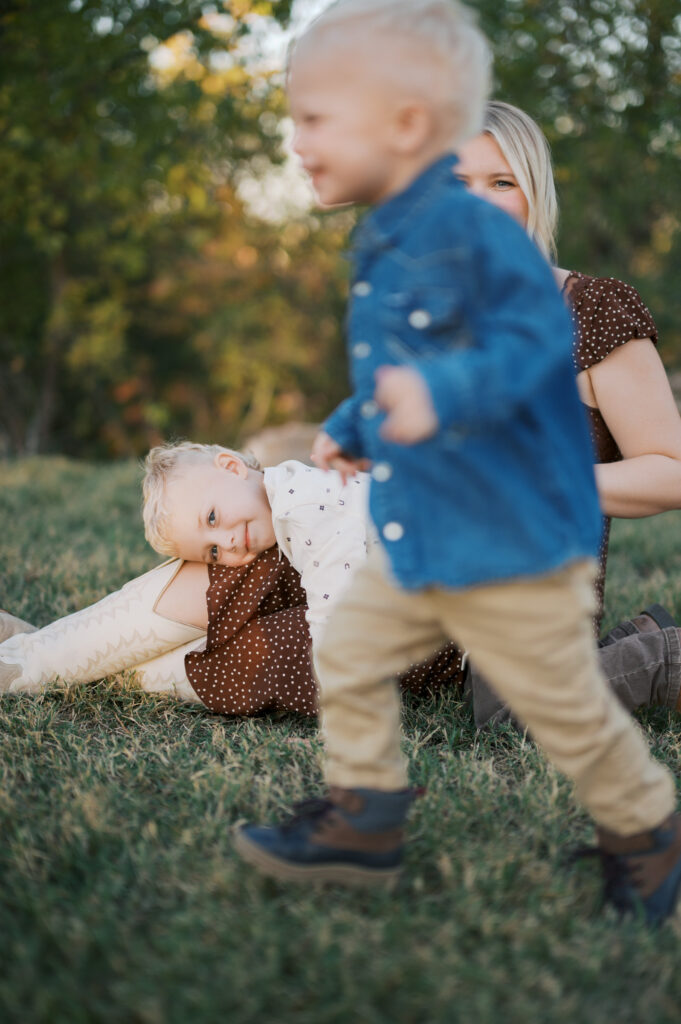 toddler boy leans on mom while other toddler runs in front during family photos with toddlers in fort worth