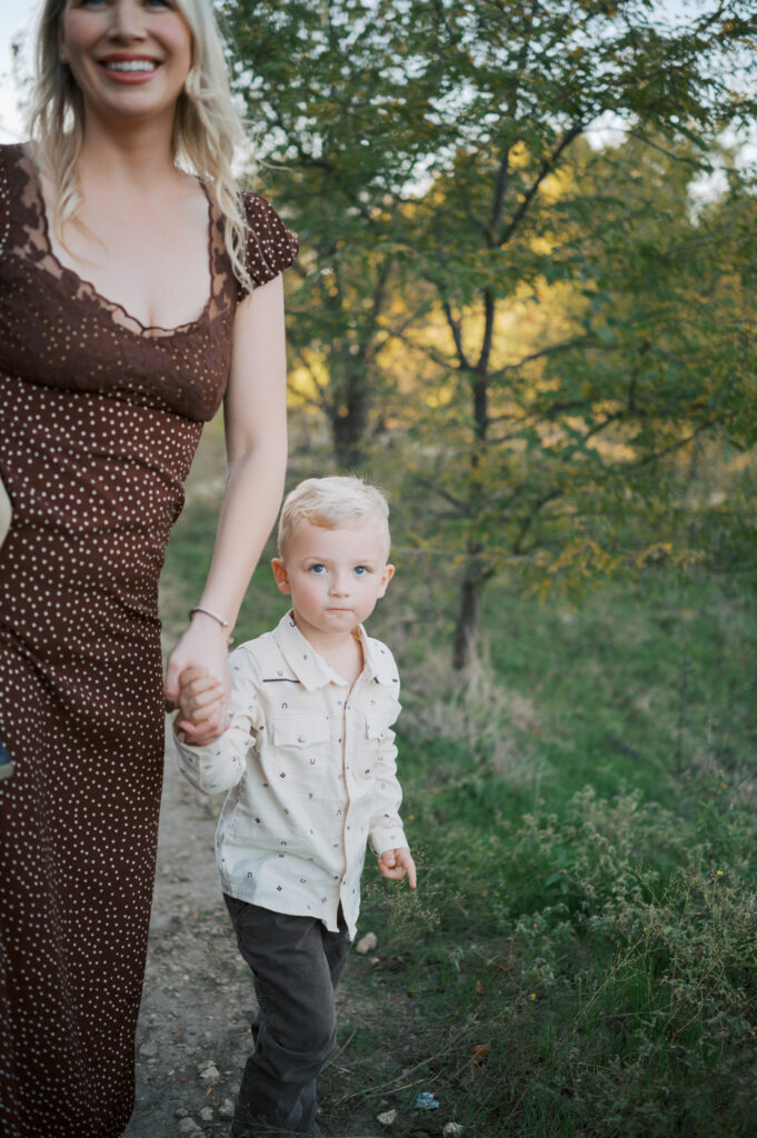 toddler looks up at camera while walking with mom outdoors during family photos