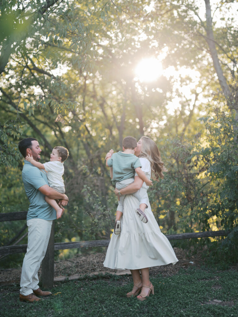 family with two little boys stands in a grassy and tree filled area during fort worth fall family photos