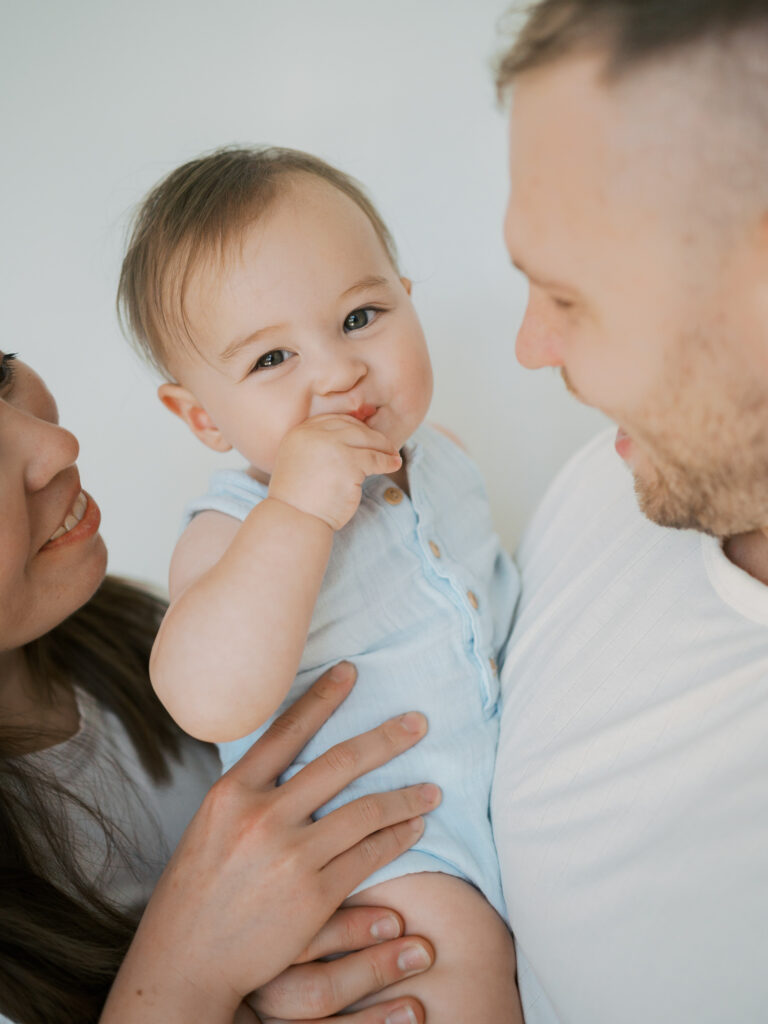 baby smiles at camera while mom and dad hold him 