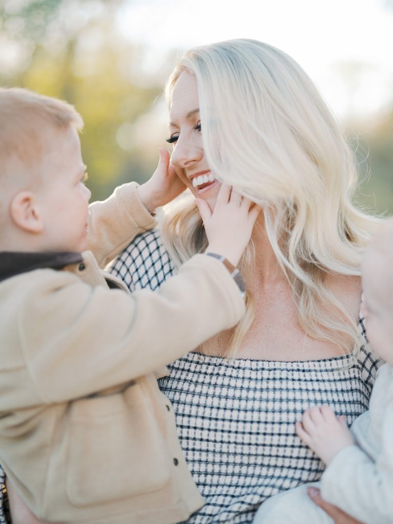 child grabs moms cheeks while mom smiles back at him