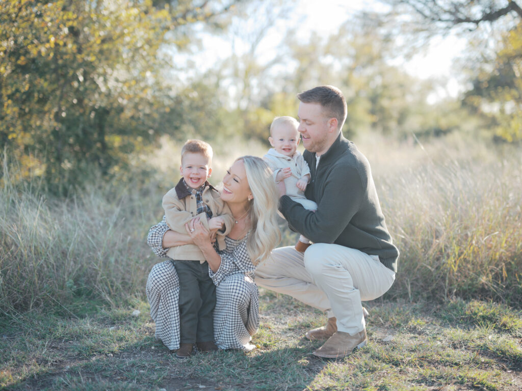 family of four kneels in grass smiling outdoors during a family photography session