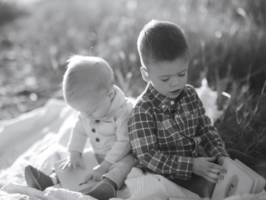 young boys sit and read books outside while sun shines on them in a black and white photo