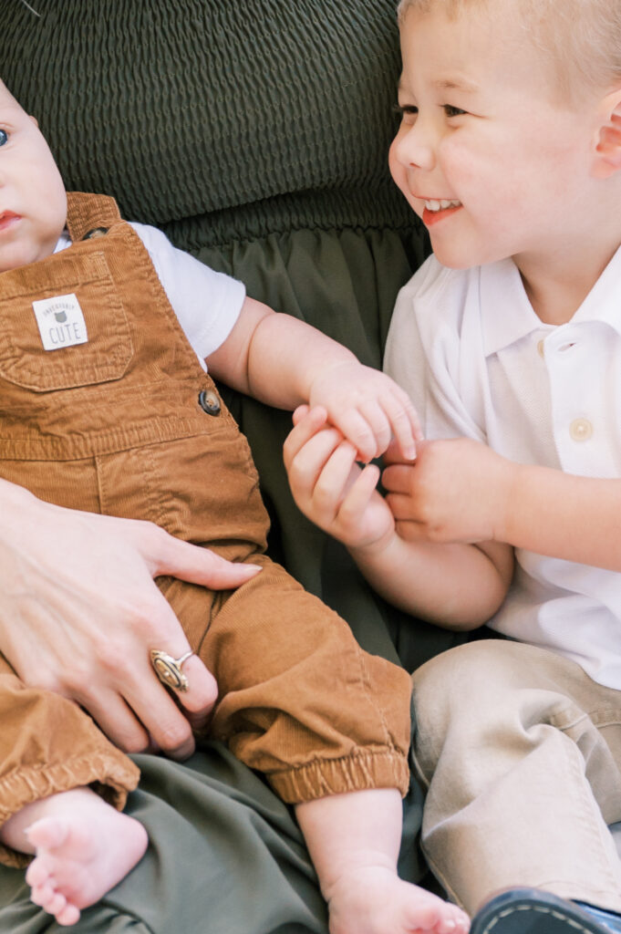 toddler boy plays with baby's hands