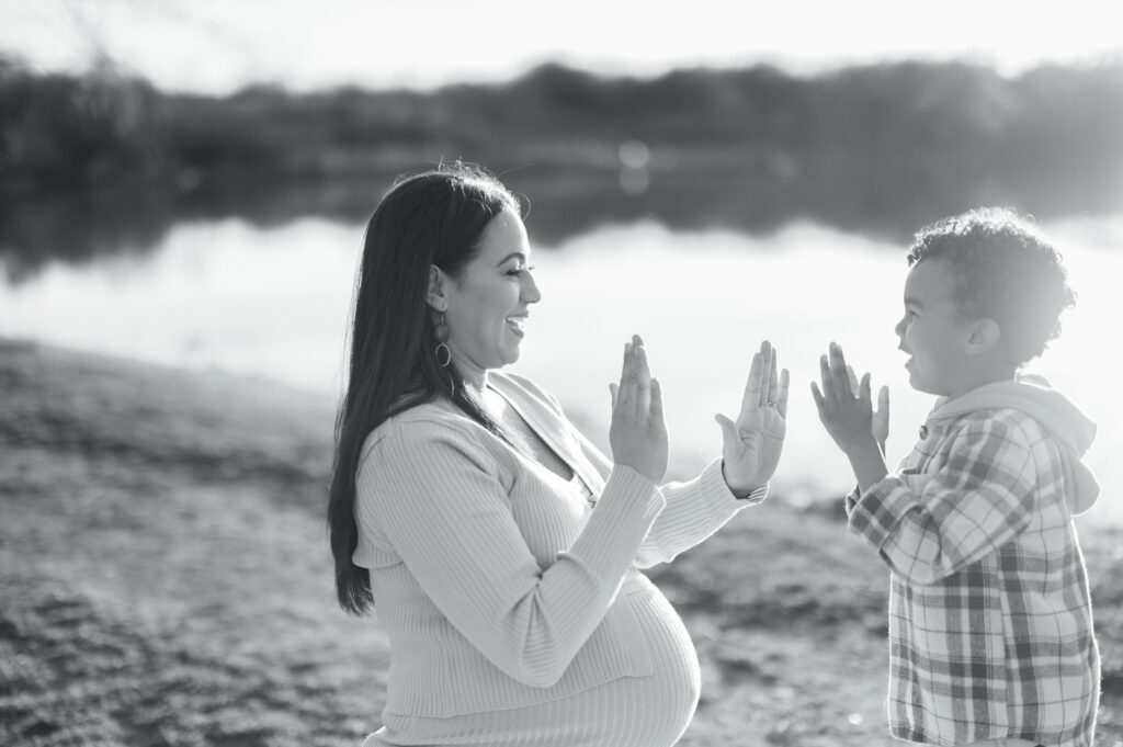 maternity session photo of son and mom playing patty cake with pond in background