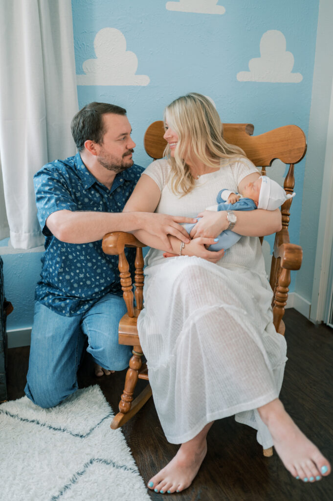mom and dad sit on a rocking chair holding baby during in-home newborn session