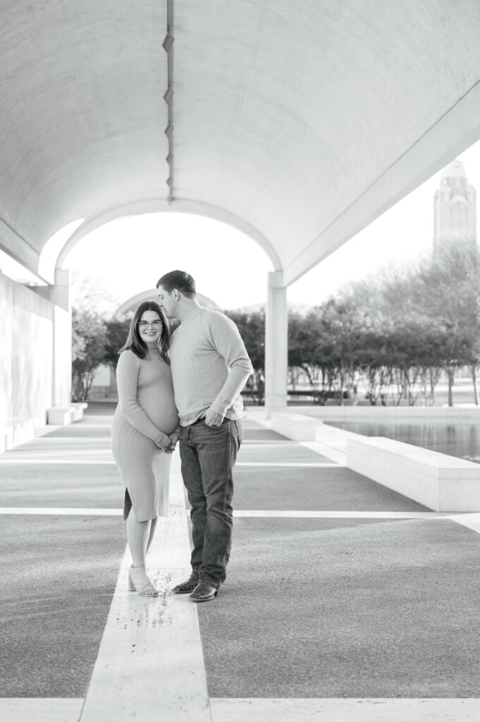 mom smiles while dad kisses her head while she holds her baby bump - fort worth photographer