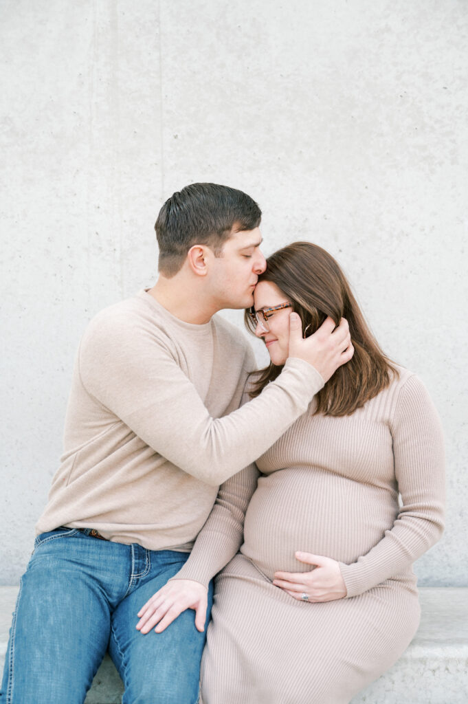 fort worth photographer captures husband kissing expecting mom while they sit on a bench