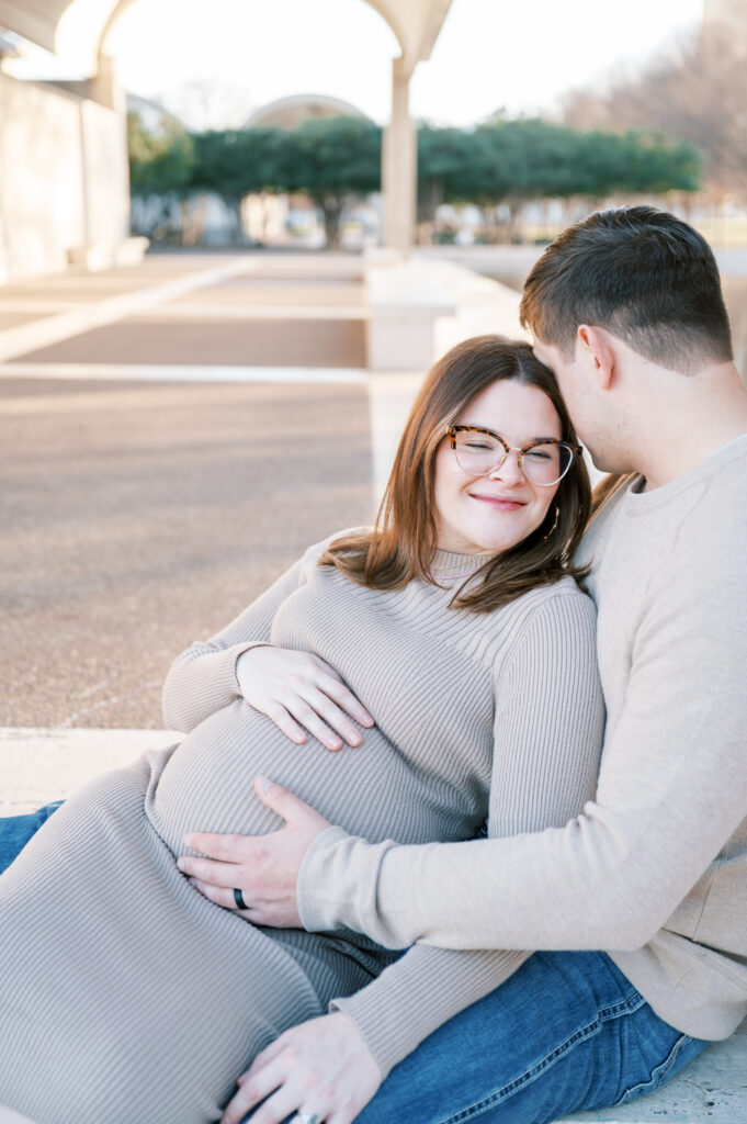 expecting mom leans into husband while they both embrace baby bump