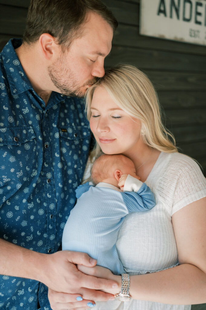 mom and dad snuggle close while mom holds baby boy during in-home newborn session